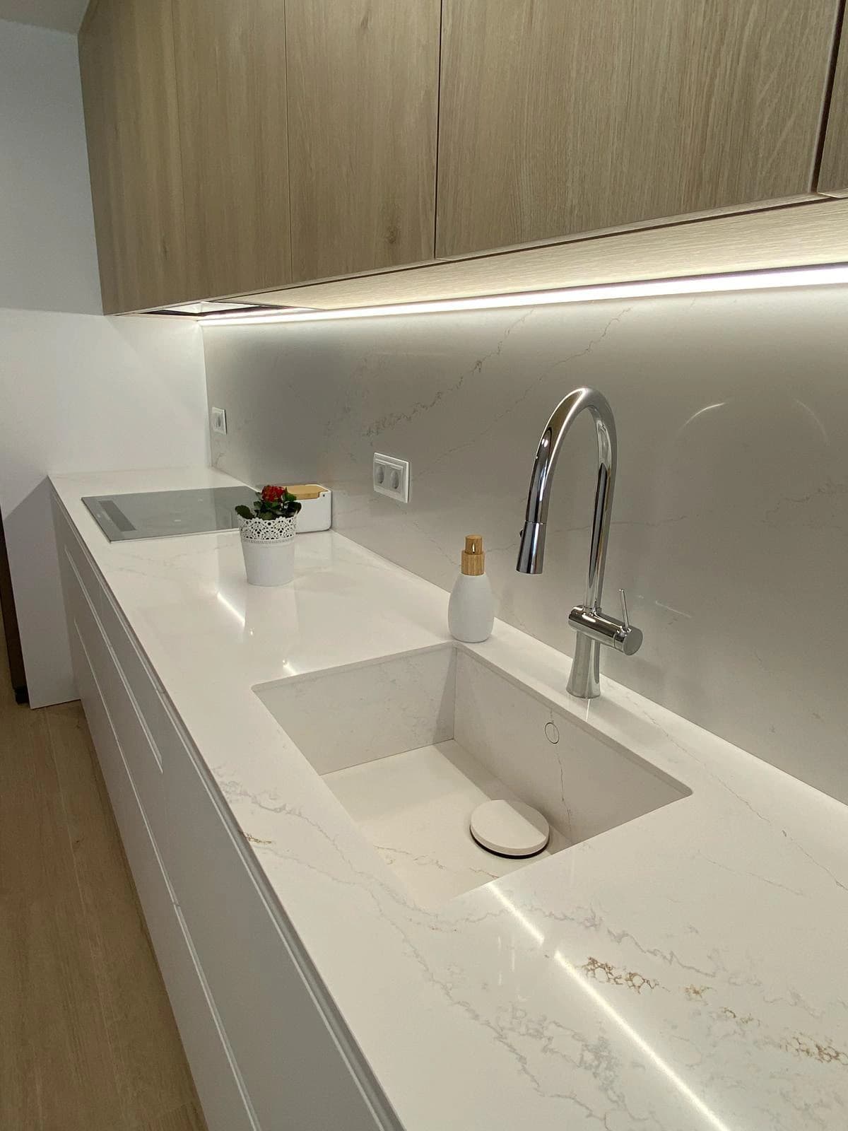 Detalle del fregadero blanco integrado en la encimera, con grifo cromado y frente de pared del mismo material.
